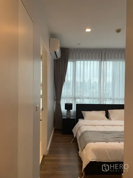 Condominium for rent or sale in Watthana, Bangkok - Entrance to the master bedroom with large windows, bedside table and en-suite door.