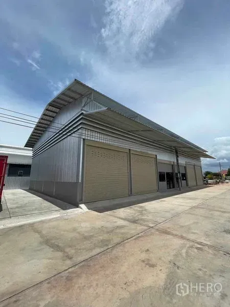 Warehouse for rent in Phra Samut Chedi, Samut Prakan - Corner view of a metal‑clad warehouse block with closed rolling doors and a truck‑friendly access road.
