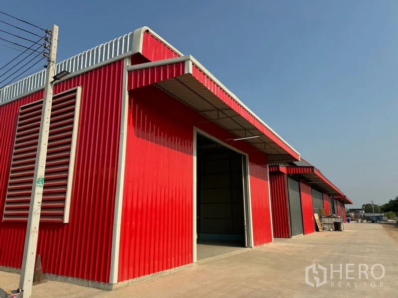 货栈 出租在Lam Luk Ka, Pathum Thani - 红灰相间的多间仓库排屋，侧墙通风百叶，沿道路排列。