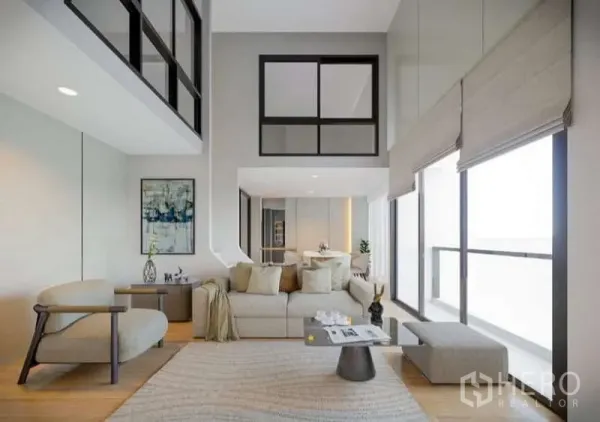Condominium for rent in Huai Khwang, Bangkok - Bright double-height living room with large windows, neutral sofa and mezzanine glazing in a modern condo.