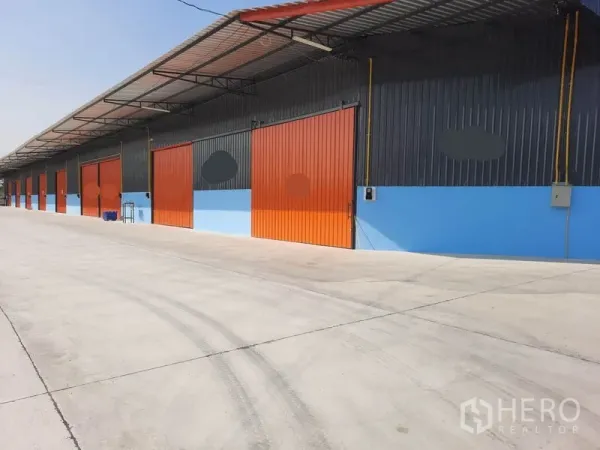 货栈 出租在Khlong Luang, Pathum Thani - 仓库外立面，橙色推拉门，带顶装卸区与宽阔混凝土车道（孔龙銮）。