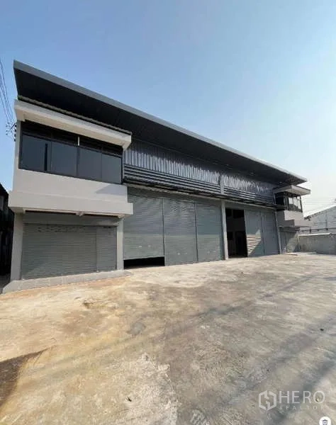Warehouse for rent in Phra Samut Chedi, Samut Prakan - Angled perspective of a long warehouse block with corner offices, canopy cover, and ample parking and turning space.