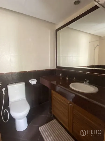 Condominium for rent - Bathroom with large mirror, dark stone countertop vanity, toilet and tiled walls.