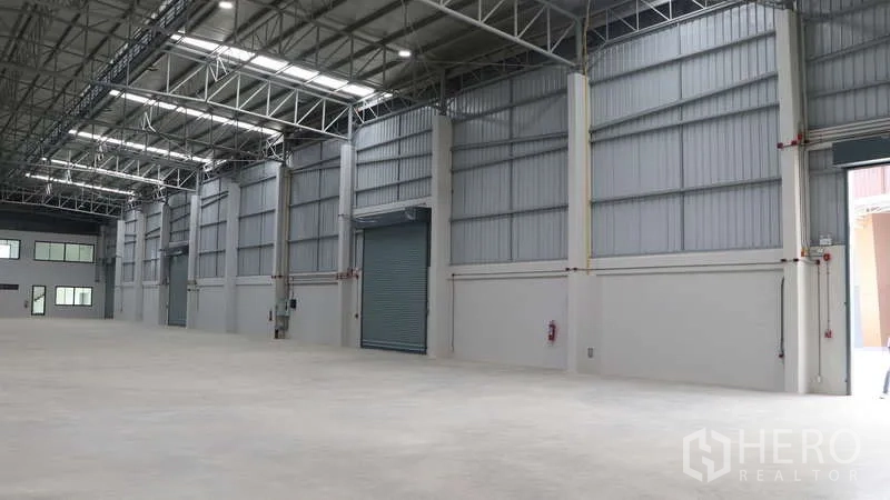 Warehouse for rent in Sam Phran, Nakhon Pathom - Bright modern warehouse interior with high ceilings, steel trusses, multiple roller shutter doors and polished concrete floor in Sam Phran.
