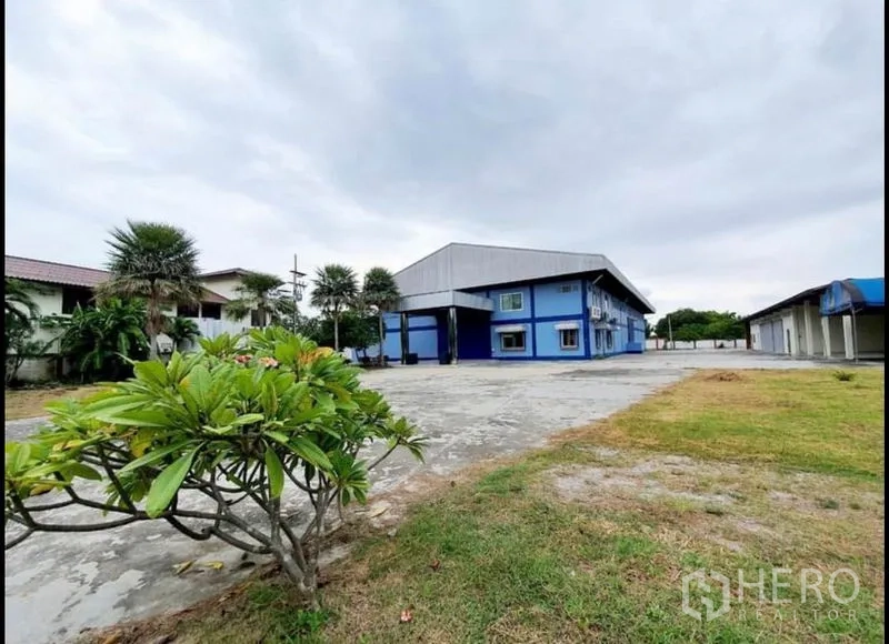 工厂 出售在Chon Buri - 蓝色工厂外观，宽阔混凝土院子与草地，阴天景致