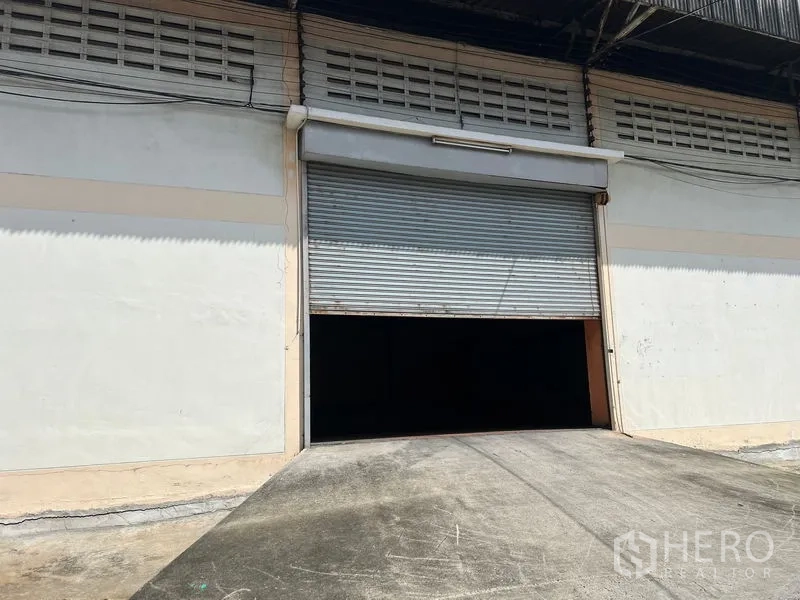 Warehouse for rent in Mueang Samut Prakan, Samut Prakan - Front facade of the warehouse with a wide roller shutter door and loading ramp.