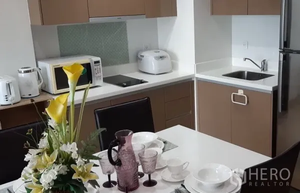 คอนโด ให้เช่าในKhlong Toei, Bangkok - ครัวเปิดท็อปสีขาว พร้อมเตาไมโครเวฟ หม้อหุงข้าว อ่างล้างจาน และตู้เย็น ข้างโต๊ะอาหาร