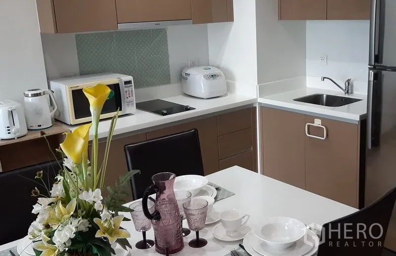 คอนโด ให้เช่าในKhlong Toei, Bangkok - ครัวเปิดท็อปสีขาว พร้อมเตาไมโครเวฟ หม้อหุงข้าว อ่างล้างจาน และตู้เย็น ข้างโต๊ะอาหาร