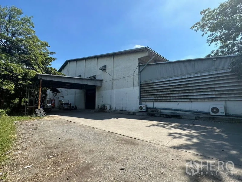 Warehouse for rent in Suan Luang, Bangkok - Warehouse exterior with covered loading bay and wide driveway under a clear blue sky.