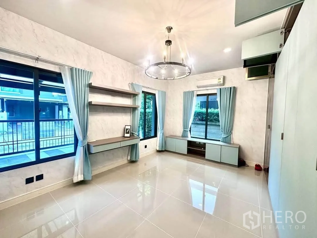 Detached House for rent in Bang Kapi, Bangkok - Bright room with large windows, pale blue curtains, wall shelves and a media cabinet.