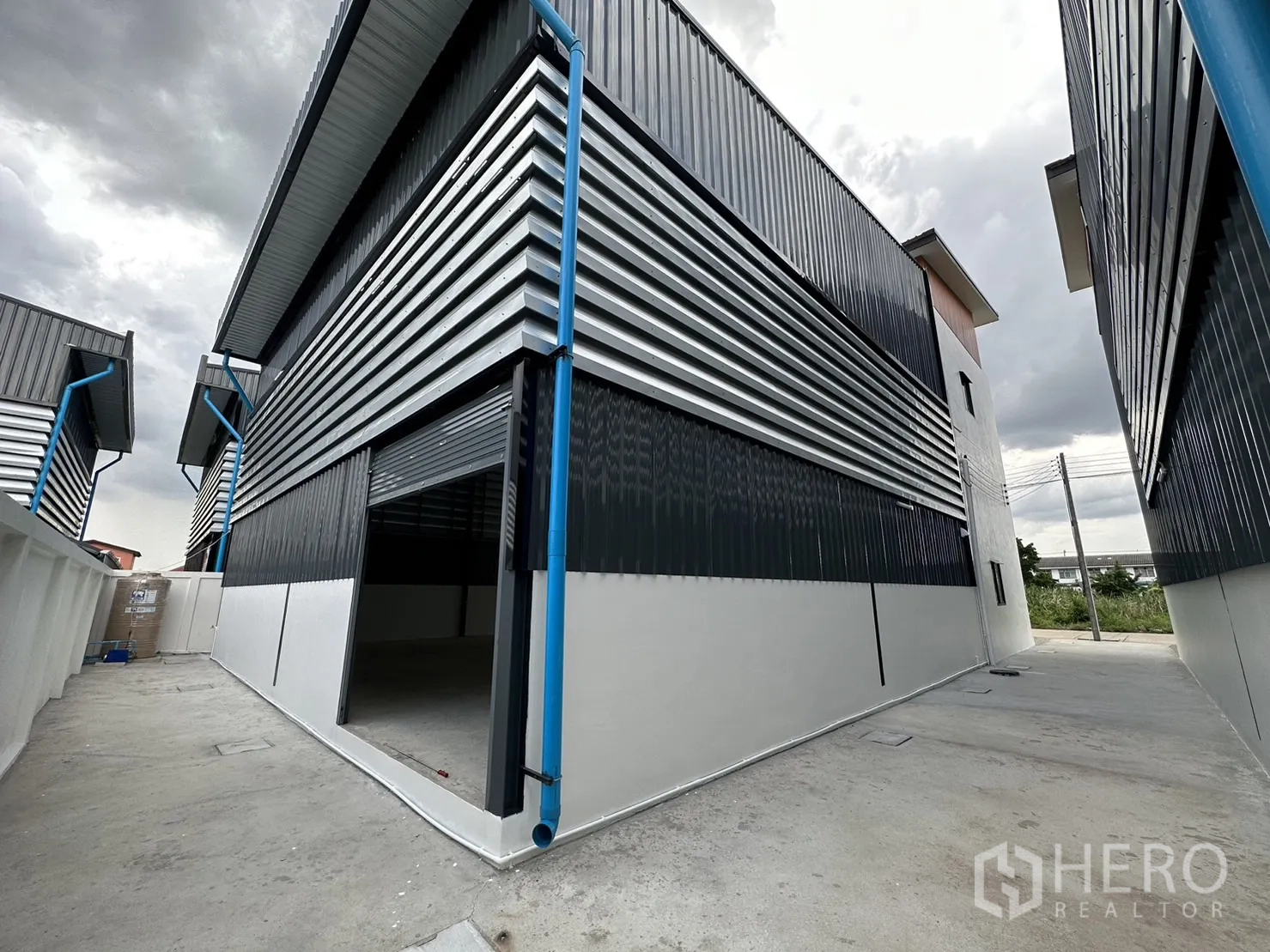 Warehouse for rent or sale - Side and rear service lane beside corrugated metal cladding and drainage.