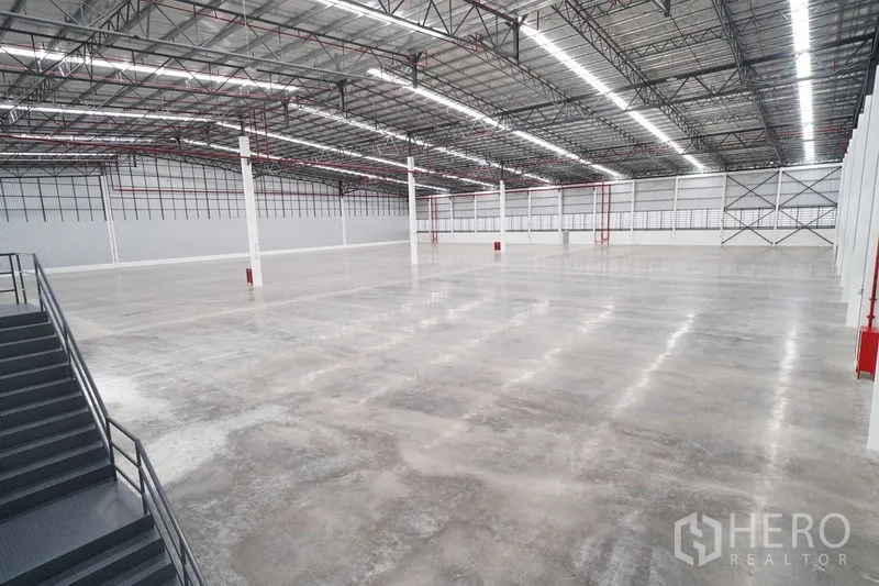 Warehouse for rent in Khlong Luang, Pathum Thani - Expansive warehouse interior with polished concrete floor, steel truss roof, LED lighting, and a side staircase.