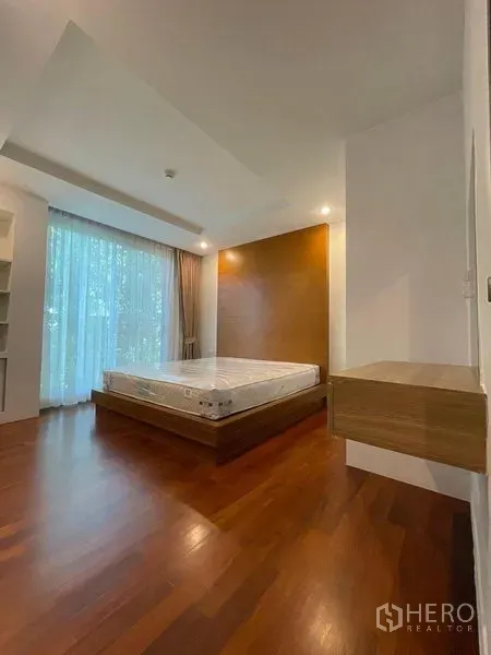 Condominium for rent in Watthana, Bangkok - Bright bedroom with platform bed, wood flooring, accent wall and floor-to-ceiling sheer curtains.
