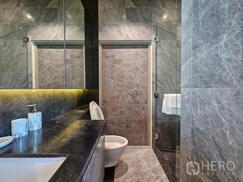 Condominium for rent - Modern gray marble bathroom with long vanity, toilet, and a glass shower door.