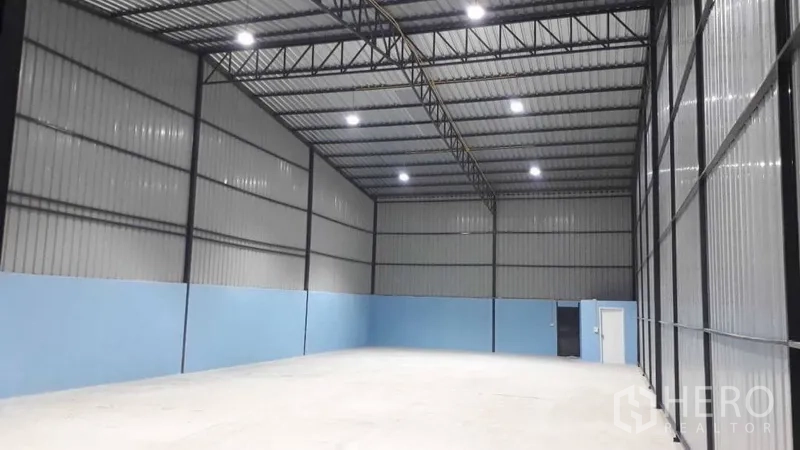 คลังสินค้า ให้เช่าในPak Kret, Nonthaburi - พื้นที่โกดังแบบโอเพ่นแพลน ผนังทาสีฟ้า ประตูบานเลื่อนขนาดใหญ่ พร้อมประตูทางคนเข้าออก