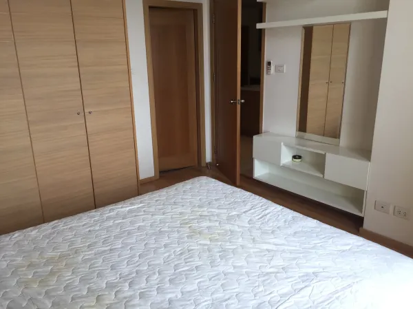 Condominium for rent in Sathon, Bangkok - Bedroom in Sathon condo with built-in wood wardrobes, dressing console and a white bed.