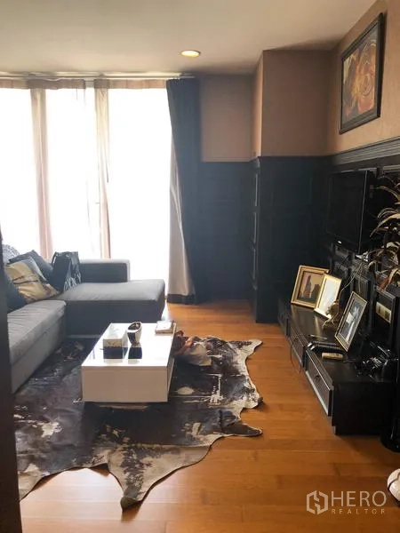 Condominium for rent in Pathum Wan, Bangkok - Sunlit living room with gray sofa, white coffee table, cowhide rug and TV console on hardwood floors.