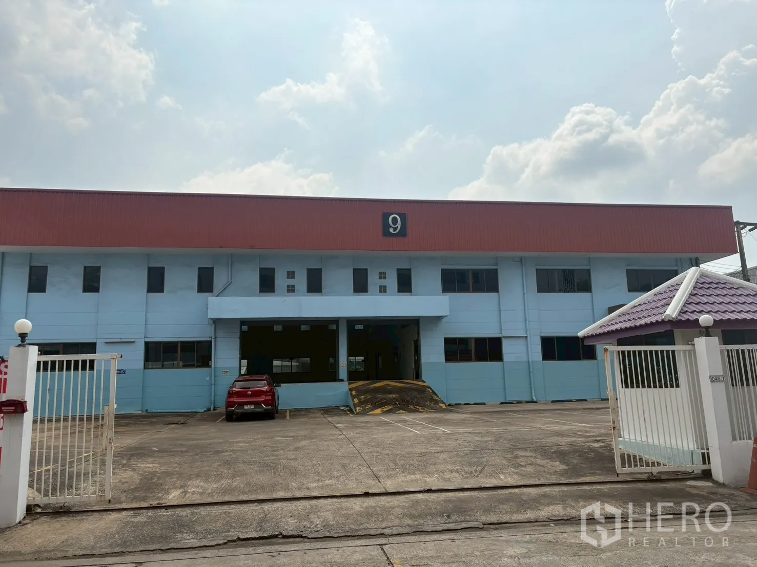 คลังสินค้า for rent in Phra Khanong, Bangkok - ประตูรั้วทางเข้าและลานจอดรถขนาดใหญ่หน้าตัวอาคาร พร้อมช่องโหลดสินค้าและทางลาด.