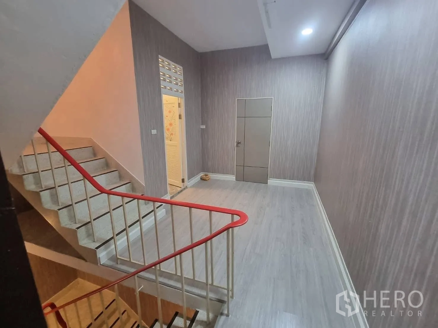 Townhouse for rent in Din Daeng, Bangkok - Staircase with red handrail leading to a wood-look landing and hallway.