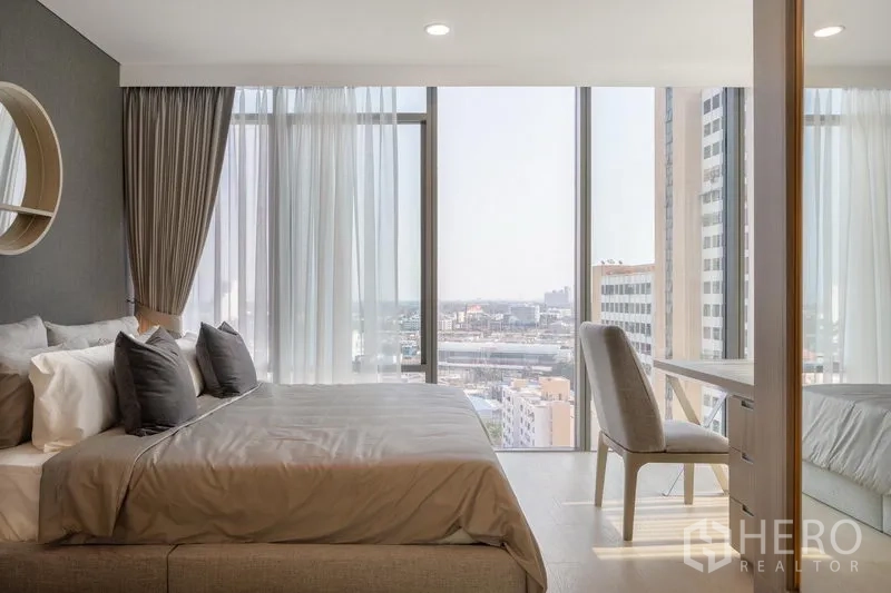 Condominium for rent in Khlong Toei, Bangkok - Corner master bedroom with floor-to-ceiling windows, desk, and expansive city skyline views.