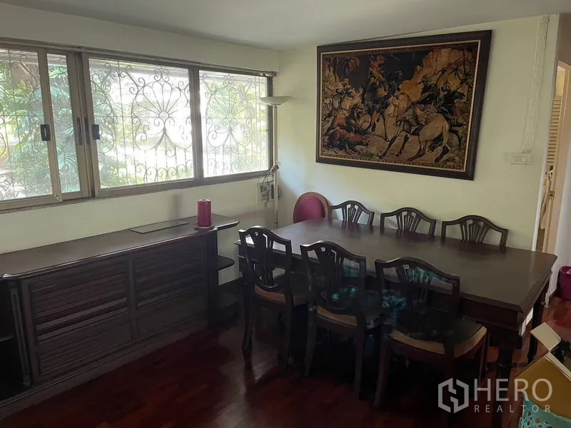 สำนักงานที่บ้าน ให้เช่าในWatthana, Bangkok - มุมรับประทานอาหาร โต๊ะไม้ยาว ตู้ข้างหน้าต่างเหล็กดัด และภาพติดผนัง