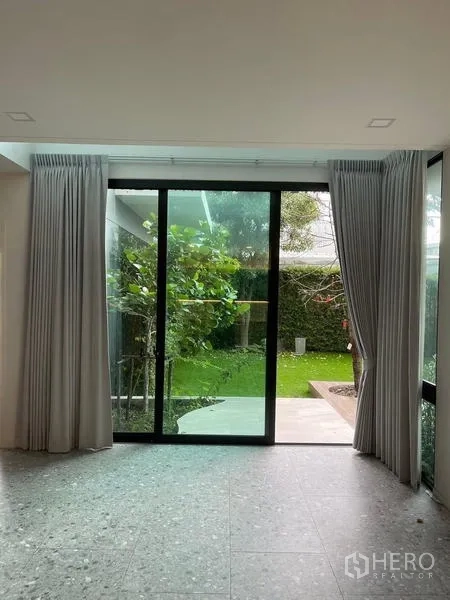 Detached House for rent or sale in Saphan Sung, Bangkok - Sliding glass doors opening to a landscaped lawn and garden with curtains drawn.