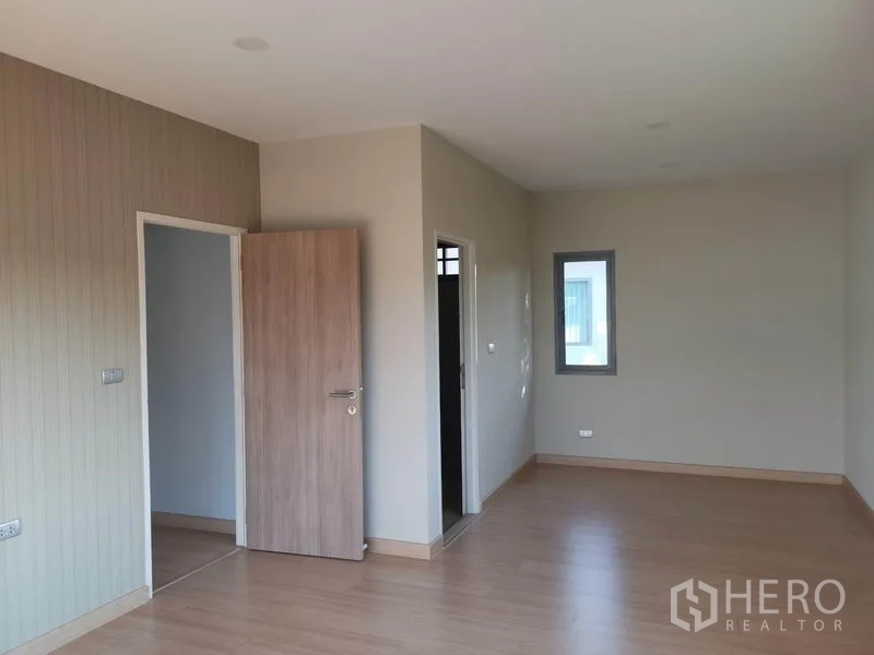 Detached House for sale in Nonthaburi - Open master-suite area with wood floors, multiple doorways and a small window.