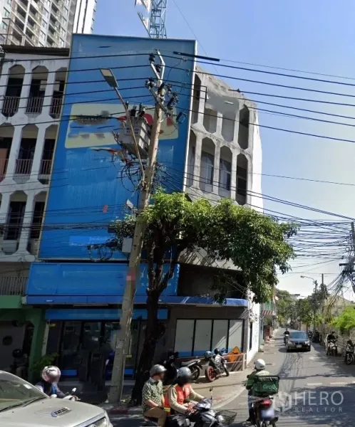 店屋 出租在Watthana, Bangkok - 转角4.5层店屋，底层玻璃门面与侧街，前方有电线与绿树，靠近BTS Ekkamai的街景。