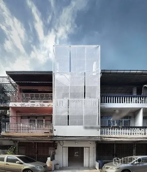 店屋 出租在Phra Khanong, Bangkok - 店屋外立面，白色穿孔金属屏风夹在街排建筑之间，天空晴朗。