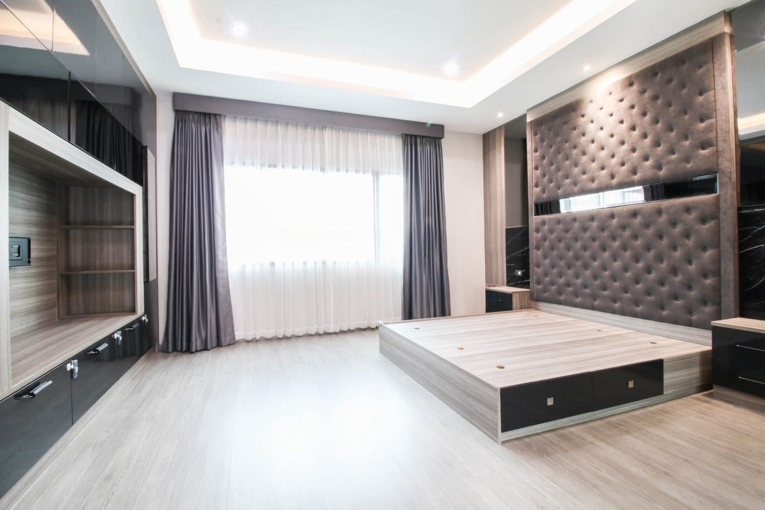 联排别墅 出租或出售在Lat Phrao, Bangkok - 主卧带抬高床台、软包背景墙、吊顶灯带与大窗帘窗。