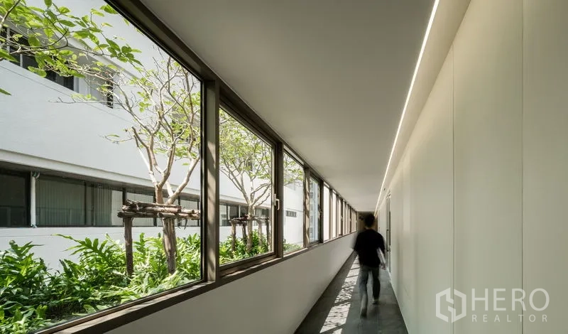 Office Space for rent in Bang Kapi, Bangkok - Interior corridor with long windows overlooking a landscaped courtyard of trees.