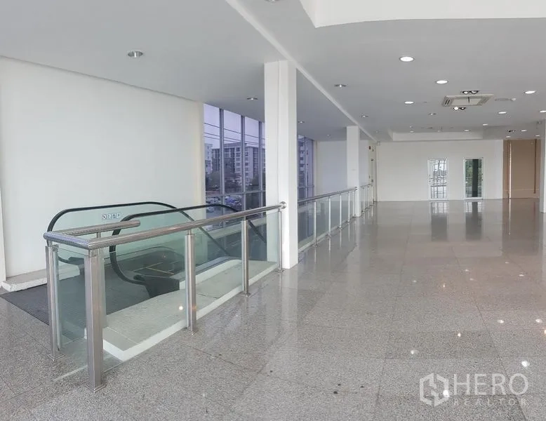 Retail Space for rent in Prawet, Bangkok - Upper level landing with glass balustrade beside an escalator leading to the retail floor.