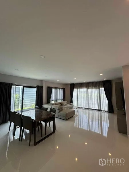Detached House for rent in Don Mueang, Bangkok - Living and dining room with glossy white floors and long curtains.