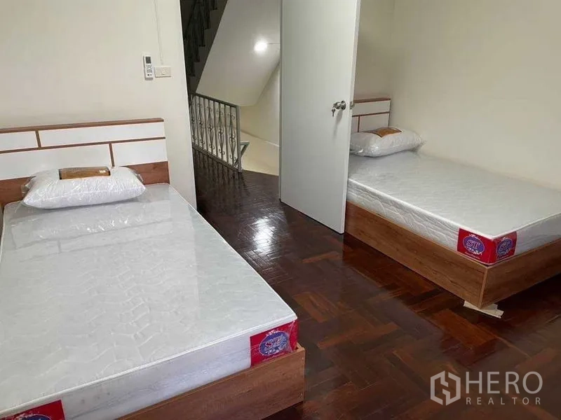 Home Office for rent or sale in Watthana, Bangkok - Twin-bed bedroom near the staircase with polished parquet floors and white walls.