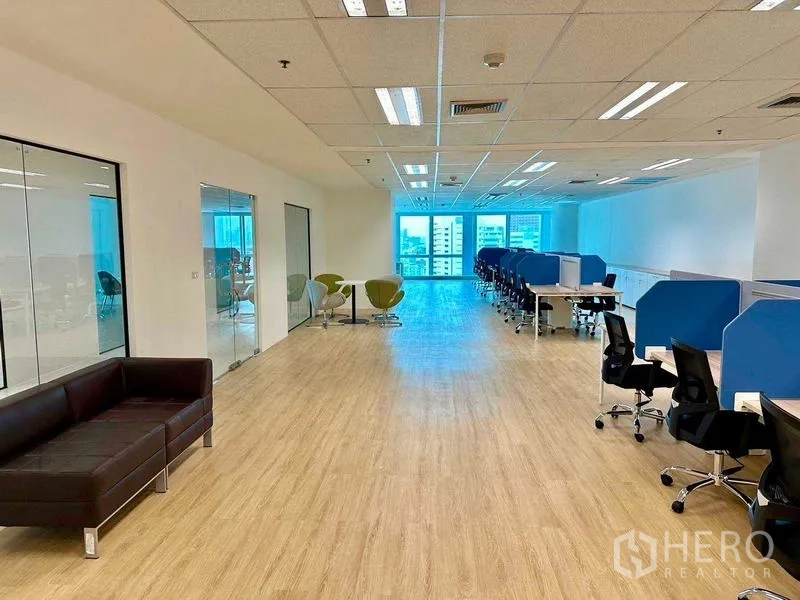 Office Space for rent - Bright open-plan office with wood floors, glass meeting rooms, lounge seating, and city-facing windows.