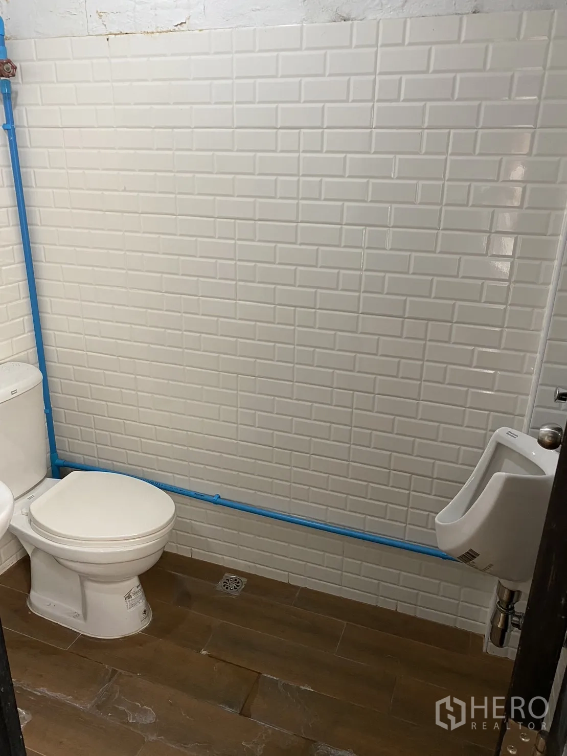 พื้นที่ขายปลีก ให้เช่าในPhaya Thai, Bangkok - ห้องน้ำปูกระเบื้องซับเวย์สีขาว พร้อมโถสุขภัณฑ์ โถปัสสาวะ และพื้นลายไม้ ท่อประปาสีฟ้า.