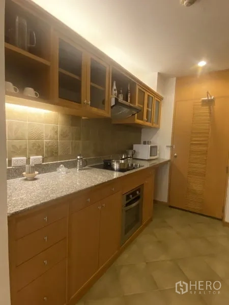 Condominium for rent - Closed kitchen with granite countertop, cooktop, range hood, microwave and glass-front cabinets.