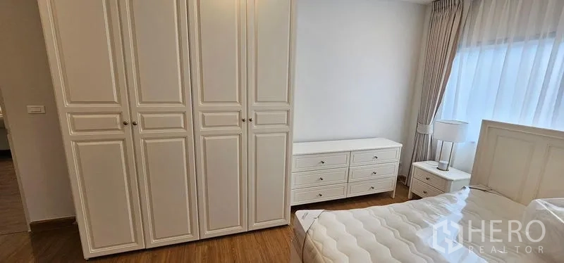 Detached House for rent - Bedroom storage view showing tall white wardrobes, dresser and bedside table near a window.