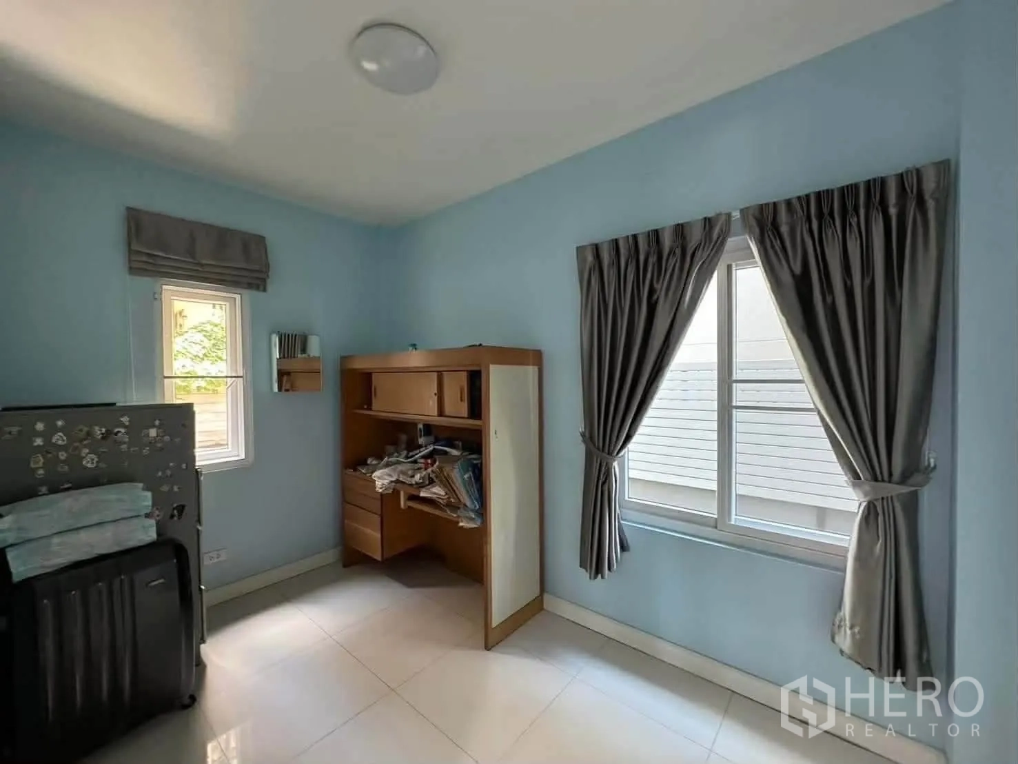 Detached House for rent in Watthana, Bangkok - Light blue room with tiled floor, desk, and two windows with curtains.
