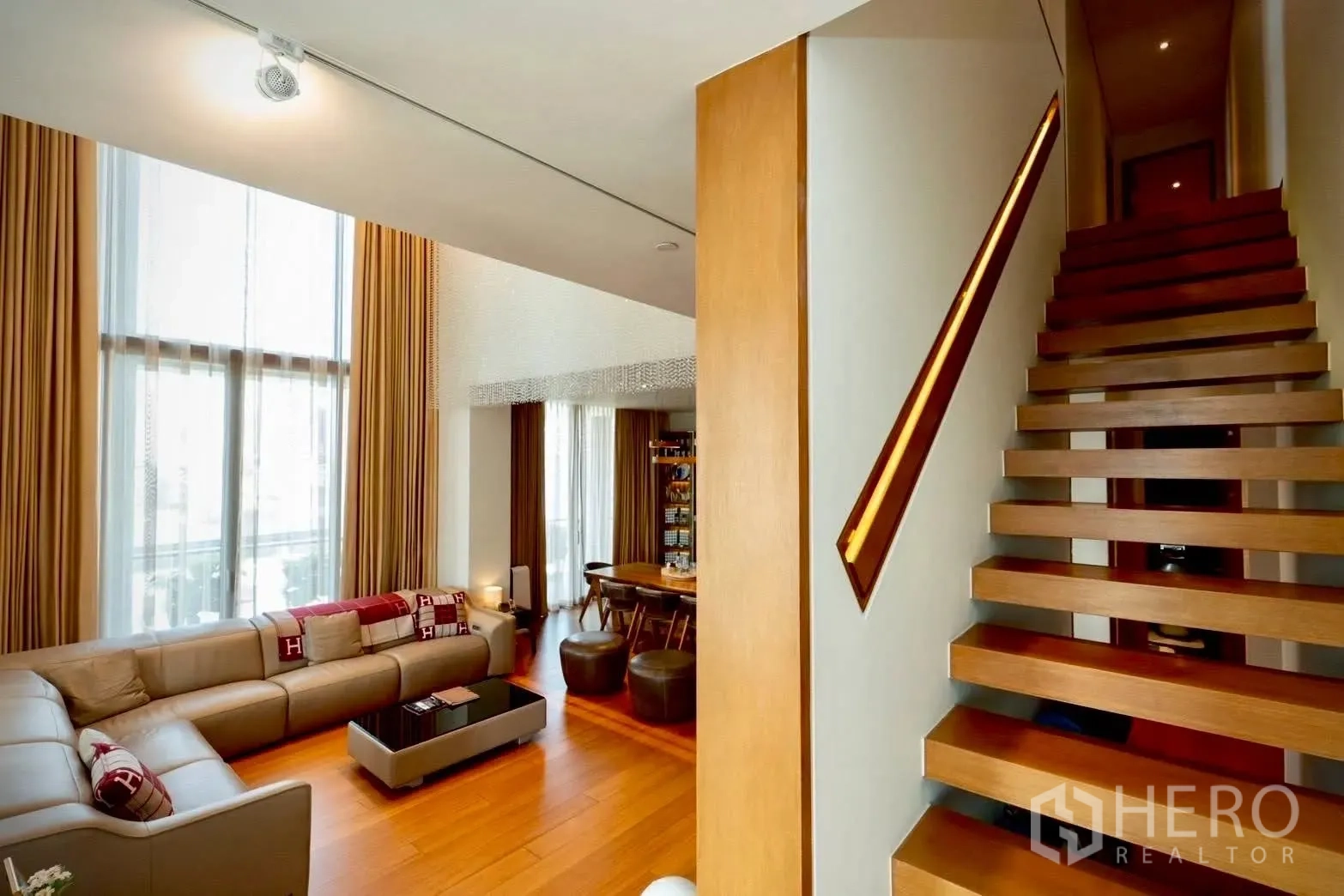 Condominium for sale in Sathon, Bangkok - Double-height living room with L-shaped sectional sofa and floating wooden staircase.