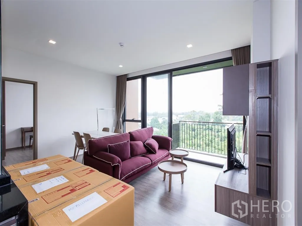 คอนโด for rent in Watthana, Bangkok - มุมนั่งเล่นโซฟาสีม่วง โต๊ะกลาง ทีวี และระเบียงมองเห็นแนวต้นไม้