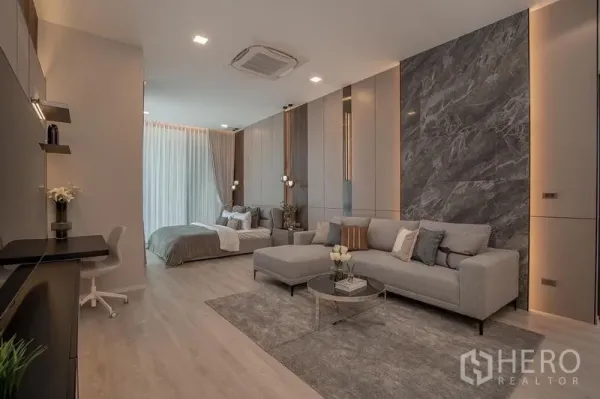 บ้าน ให้เช่า - ห้องแบบเปิดโล่ง มีโซฟานั่งเล่น โต๊ะทำงาน และเตียงนอน แสงไฟนุ่มนวล.