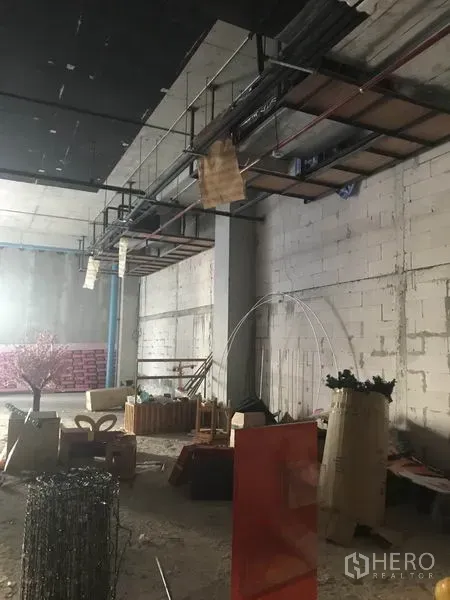 零售空间 出租在Khlong Toei, Bangkok - 毛坯零售空间，挑高天花，外露管线与混凝土砌块墙，地面堆放材料。