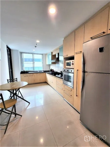 公寓 出租在Bang Rak, Bangkok - 封闭式现代厨房，浅木色橱柜、嵌入式烤箱、不锈钢冰箱、油烟机与窗边早餐角。