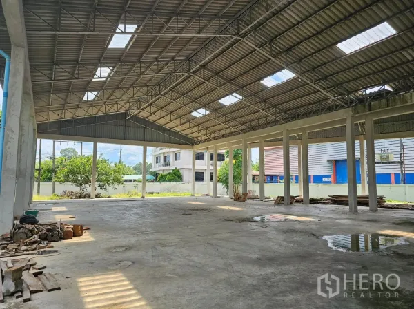 工厂 出租或出售在Mueang Rayong, Rayong - 厂房侧向半开放装卸区，高柱支撑金属屋顶，可见庭院绿植与邻近建筑。