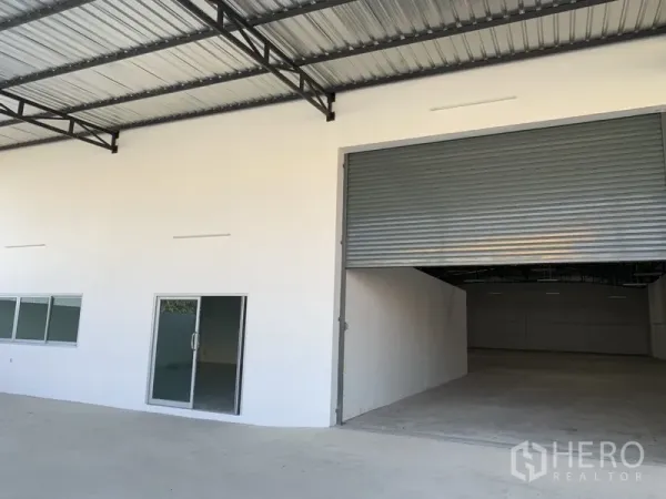 Warehouse for rent in Samut Prakan - Facade with sliding glass office door and wide roller shutter leading into the warehouse.
