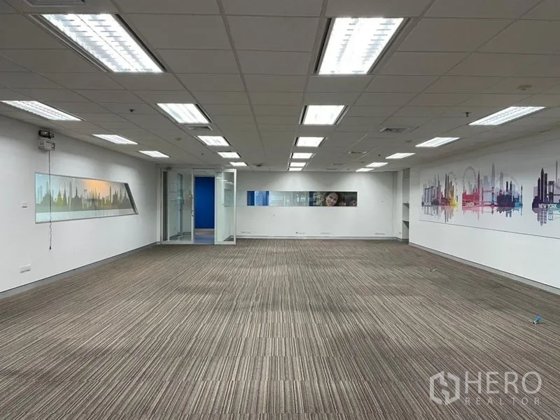 Office Space for rent - Expansive office floor with suspended light panels, a glass entry door and skyline wall graphics.