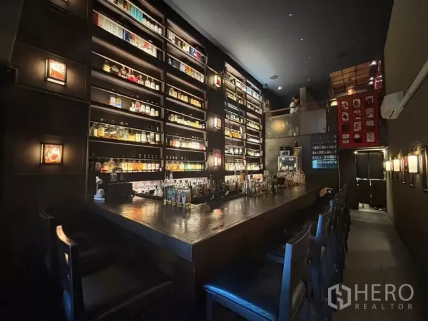 店屋 出租在Watthana, Bangkok - 灯光昏暗的酒吧，长木吧台与发光酒架，带夹层。