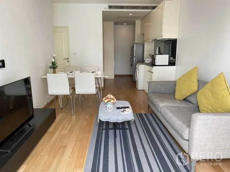 คอนโด ให้เช่าในBangkok - โถงนั่งเล่นและทานอาหารแบบโอเพ่นแพลน โซฟาสีเทา พรมลายทาง ทีวี และครัวบิลท์อิน