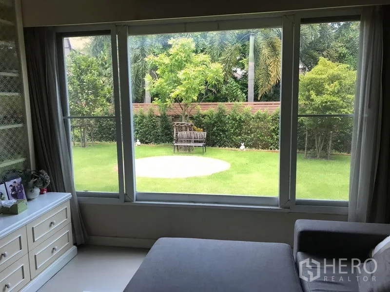 Detached House for sale in Pak Kret, Nonthaburi - Green garden viewed through wide windows, showing bench and hedge.